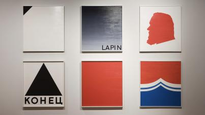Photograph of six minimalist square paintings arranged in two rows of three on a white wall, featuring geometric shapes and bold colors like black, white, red, and blue. Notable elements include Cyrillic text "КОНЕЦ" under a black triangle, gradient shading with "LAPIN" text, and a red silhouette profile, suggesting themes of abstraction and symbolism.