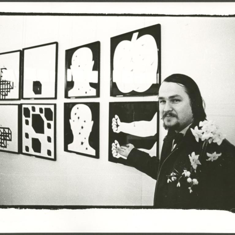 a black and white photograph of an artist pointing to his work on the wall