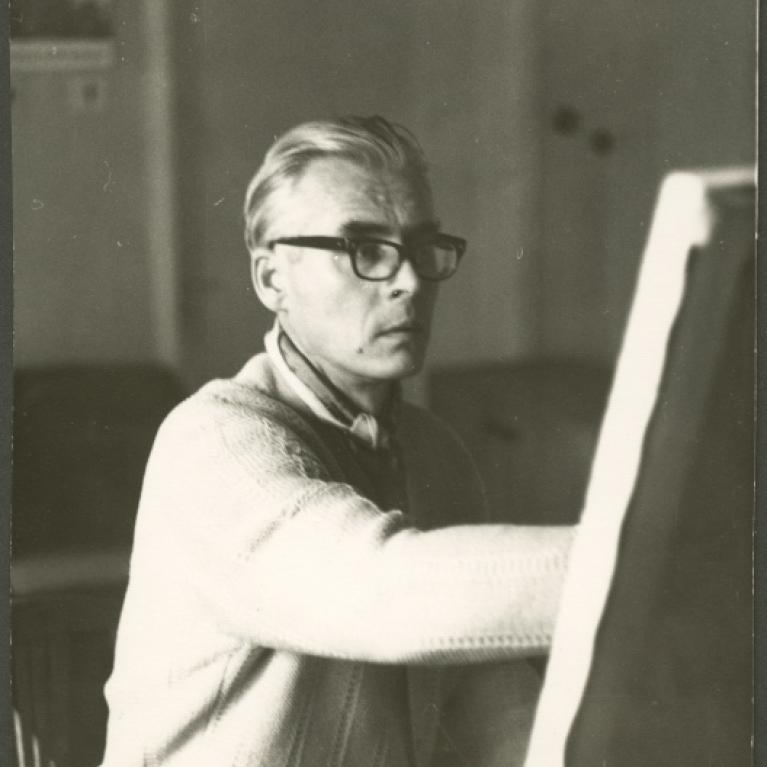 a man in glasses and cardigan in the process of painting