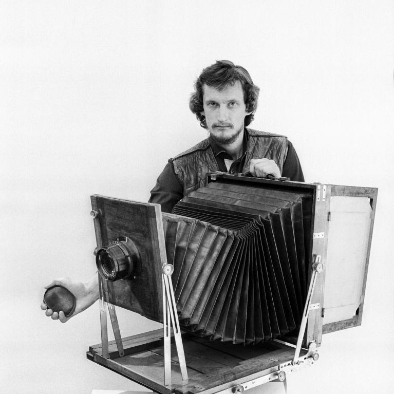 young man with longer hair and moustache in front of an early 20-th century photo camera