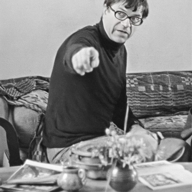 middle-aged man wearing turtleneck and glasses points to something with his right hand