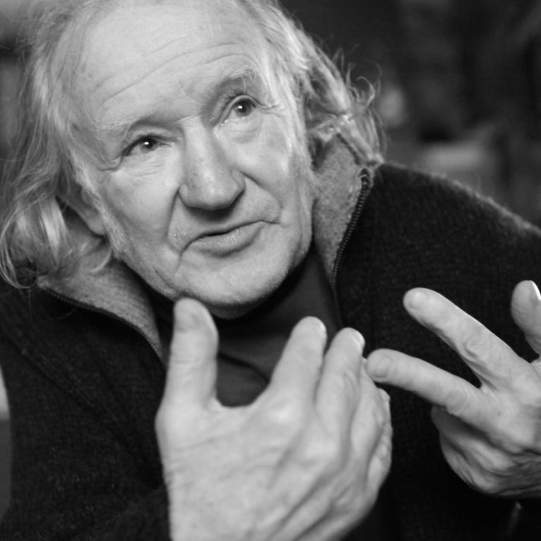an old man with long grey hair gesticulating 