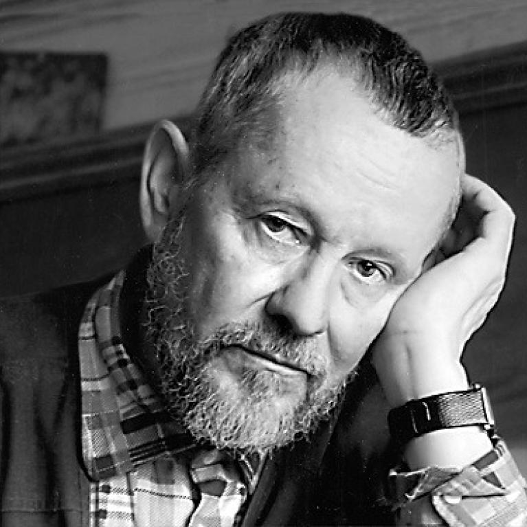 older man with beard, head on his wrist, looking into the camera