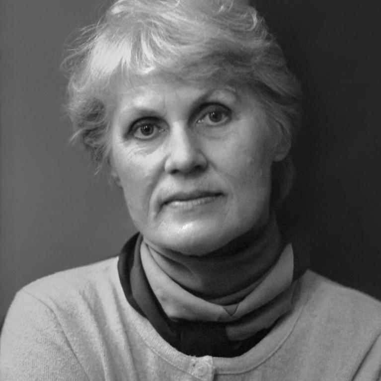 middle-aged blonde woman in a cardigan with red flag pin