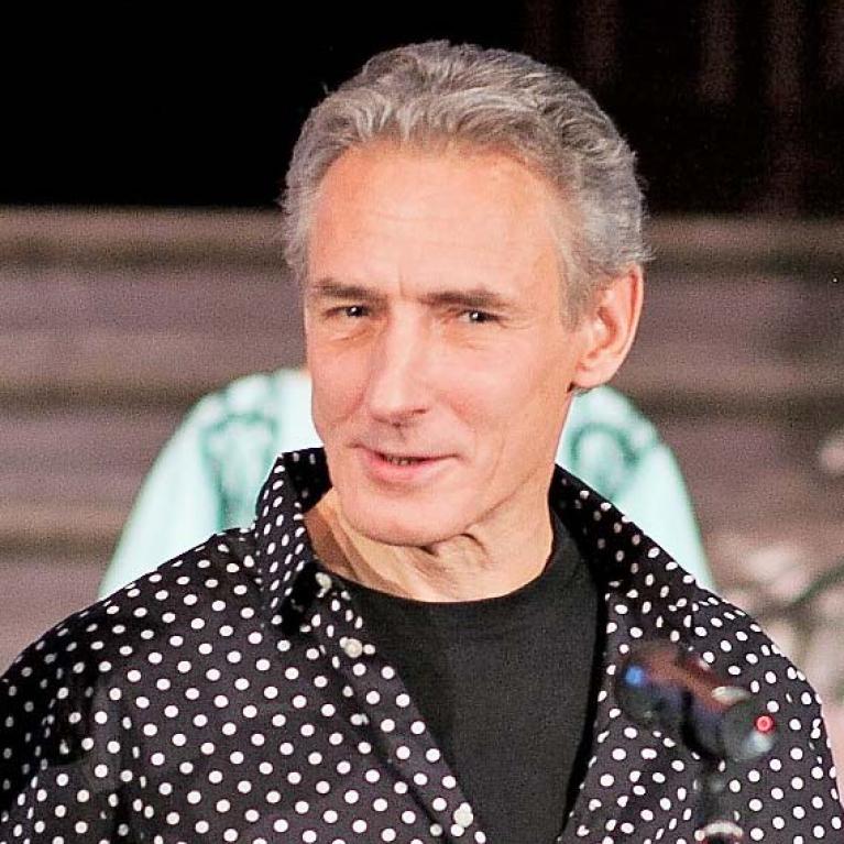 middle-aged grey-haired man in a shirt in front of a microphone