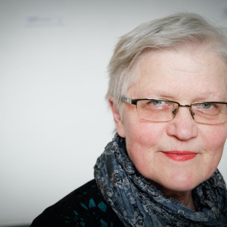 older woman with short hair wearing glasses, red lipstick, and a silk scarf