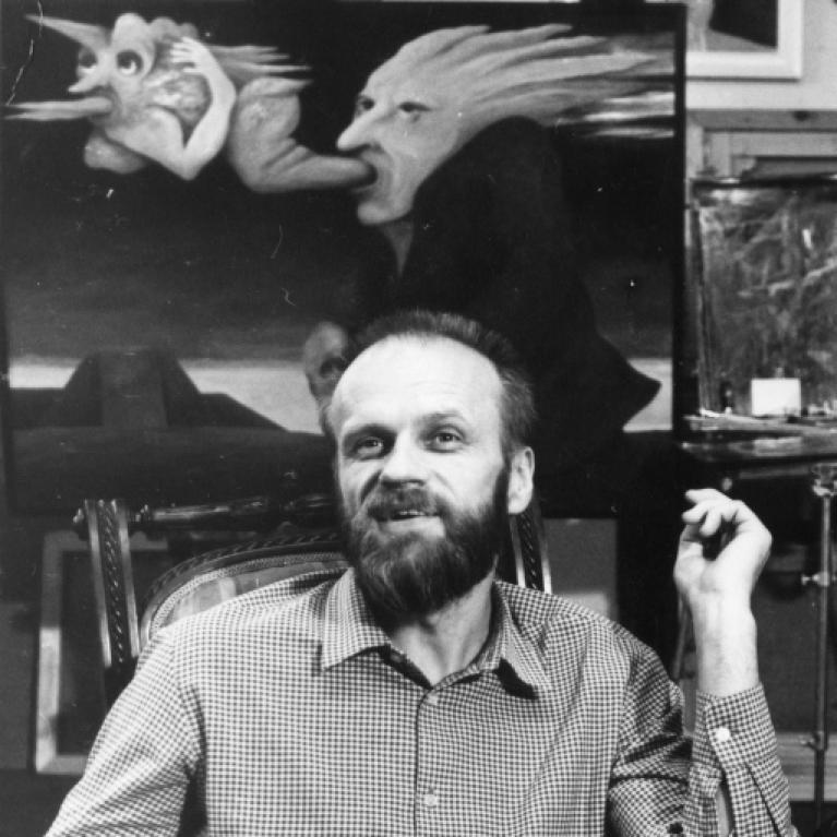 Black and white photograph of a man seated indoors with a checkered shirt, holding a cigarette in his right hand. Behind him is a painting featuring a surreal creature with a human face and bird-like features