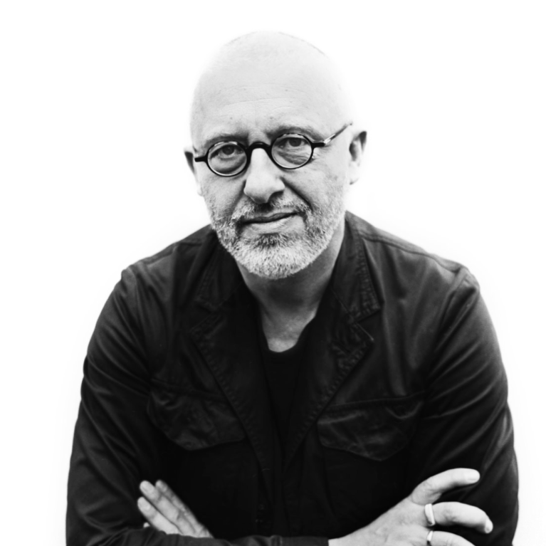 Black and white photograph of a person wearing glasses, a dark jacket and black shirt with arms crossed. 