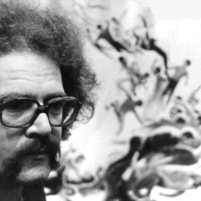 Black and white photograph showing a close-up of a person with curly hair and glasses, positioned on the left side. The background features an abstract, dynamic mural or artwork with swirling, flowing shapes and figures.