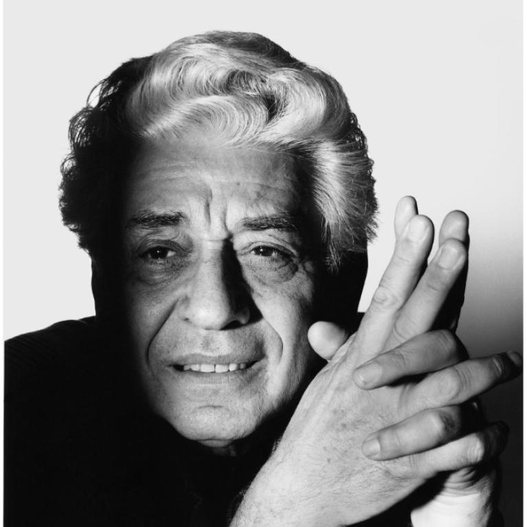 Black and white photograph of a person with curly hair, hands clasped together near the face. The photo emphasizes texture and contrast, highlighting details in hair and skin against a plain background.