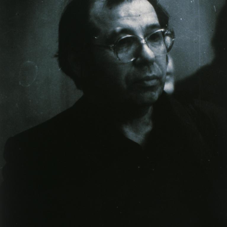 Black and white photograph of a person in profile view against a dark background, with lighting highlighting the side of their face and head. The image emphasizes contrast between light and shadow, creating a dramatic and moody atmosphere.