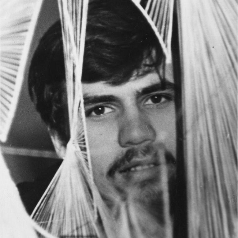 Photograph showing a person partially obscured by a geometric string art installation composed of white threads arranged in curved, intersecting patterns.