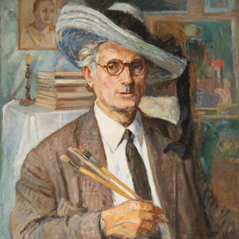 A painted portrait of a man wearing a brown suit, white shirt, and dark tie, holding paintbrushes in his right hand. Background includes a table with stacked books, a lit candle, and framed artwork, suggesting an artist's studio setting.