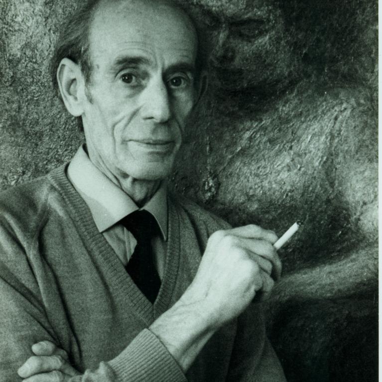 Black and white photograph of an elderly man wearing a sweater and tie, holding a cigarette in his right hand. A textured background features a faint, sculpted figure embracing the man from behind, adding a surreal and artistic element to the portrait.