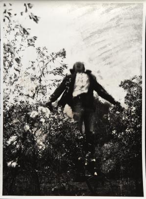 Black and white photograph showing a person mid-jump surrounded by dense foliage and plants. The figure appears blurred, emphasizing motion against a textured sky background with visible streaks.