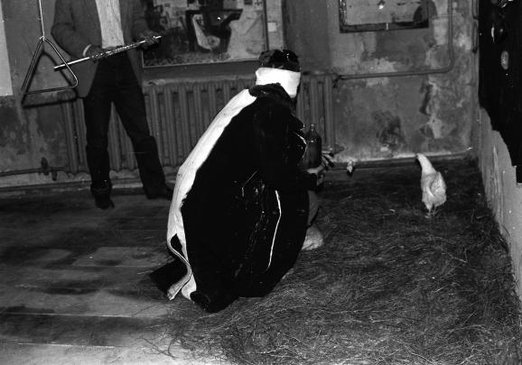 a blindfolded person in a corner of the room chasing a chicken